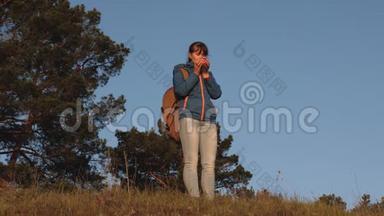 远足女孩喝热茶，看日落。 女旅行者，<strong>站在山顶</strong>上，用玻璃喝咖啡